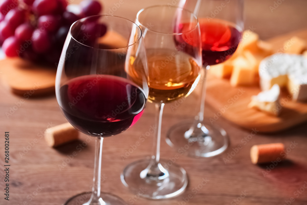 Glasses with different wines and appetizers on wooden table, closeup