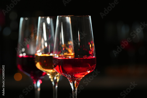 Row of glasses with different wines against blurred background, closeup. Space for text
