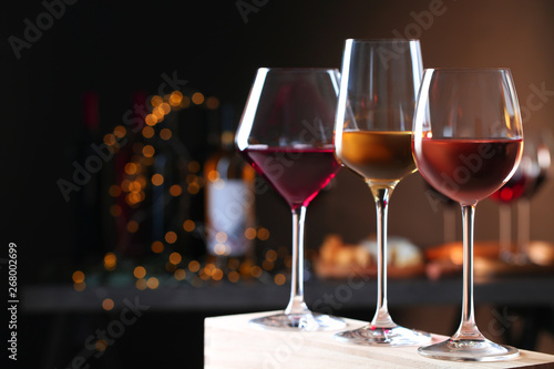 Glasses with different wines on wooden table against defocused lights. Space for text