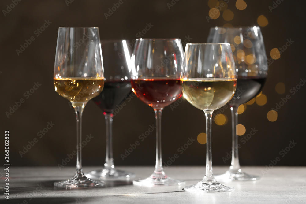 Glasses with different wines on grey table against defocused lights