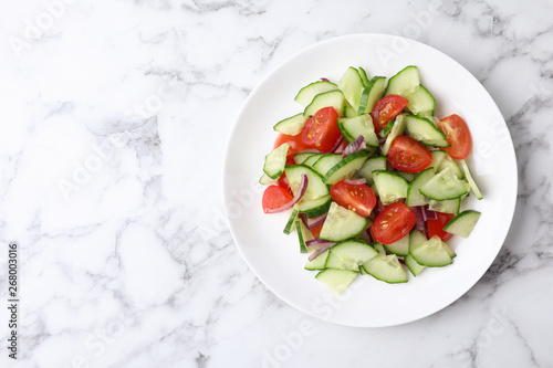 Plate of vegetarian salad with cucumber, tomato and onion on marble background, top view. Space for text