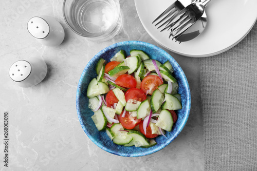 Bowl of vegetarian salad with cucumber, tomato and onion served on table, flat lay