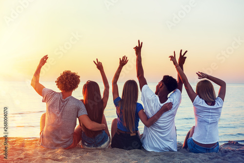 Group of happy friends having fun at ocean beach at dawn