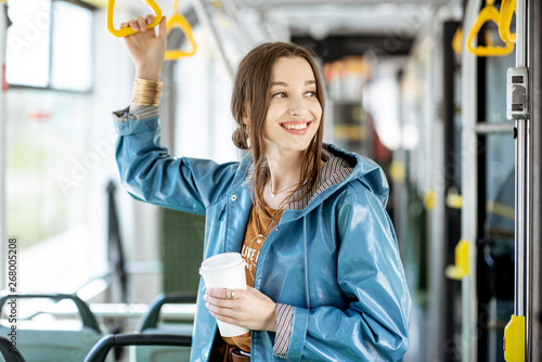 Young woman passenger enjoying trip at the public transport, standing with coffee in the modern tram photo