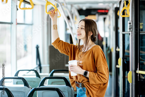 Young and happy passenger enjoying trip at the public transport, standing with coffee in the modern tram