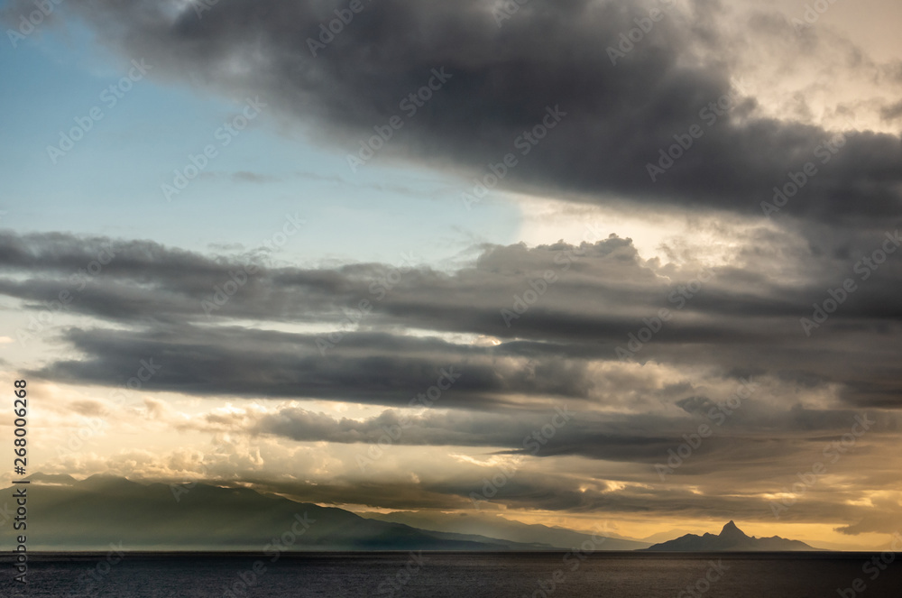 East Nusa Tenggara Island, Indonesia - February 24, 2019: Early morning at sunrise. Southside coast off Sessok in Savu Sea under cloudscape with yellow and darker patches. Dark sea, small Mules island