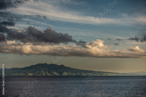 East Nusa Tenggara Island, Indonesia - February 24, 2019: Early morning at sunrise. Southside coast off Sessok in Savu Sea under cloudscape with yellow and darker patches. Dark sea and green hills
