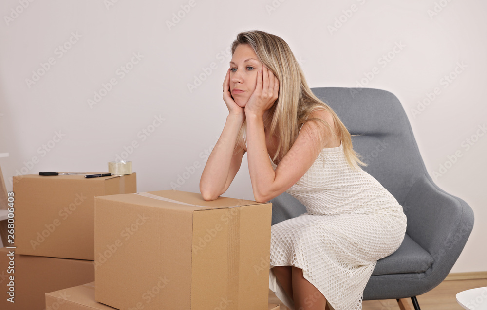 Moving in and out. Tired woman sitting next to carton boxes Moving in and out. Tired woman sitting next to carton boxes