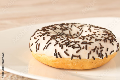 Fresh glazed donut with chocolate sprinkles on a white plate.