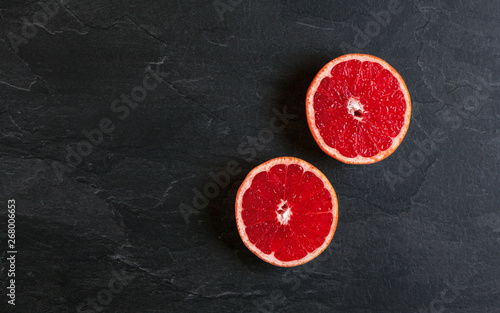 Flat lay photo - pink grapefruit cut in two halves, on black slate board