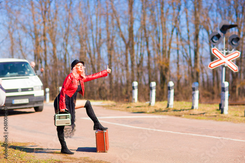 Beautiful young woman catching a car hitchhiking along the road