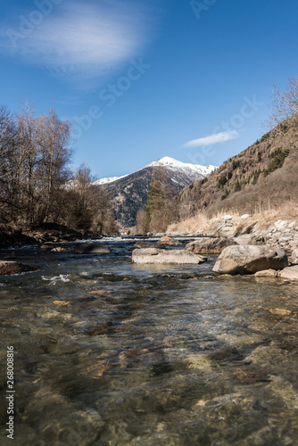 Noce River in Italian Alps. Mountain river surrounded by trees, stones and snow-capped mountains. Trento, Trentino, Italy