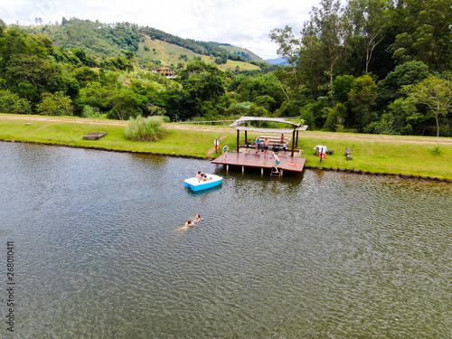 Aerial view of beautiful little wood cabana next the lake in tropical mountain, with family enjoying relax sun moment, swimming and fishing. Monte Alegre Do Sul, Brazil. 