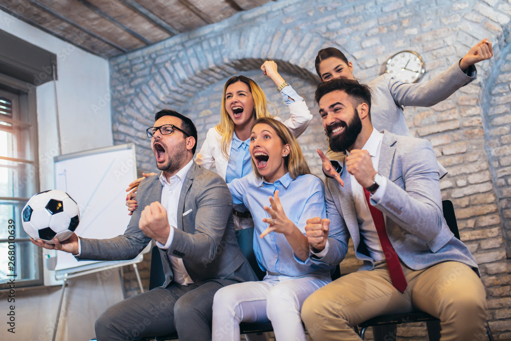 © Mediteraneo - Happy business people or football fans watching soccer on tv and celebrating victory. Friendship, sports and entertainment concept.
