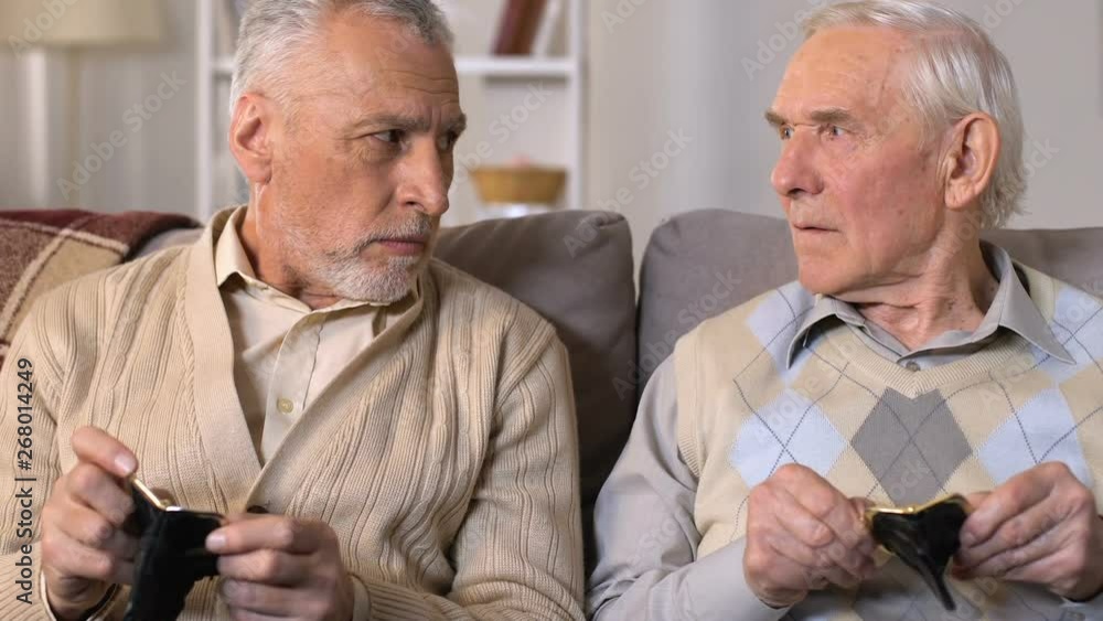 Unhappy senior males looking empty wallets, pension poverty, retirement savings Unhappy senior males looking empty wallets, pension poverty, retirement savings