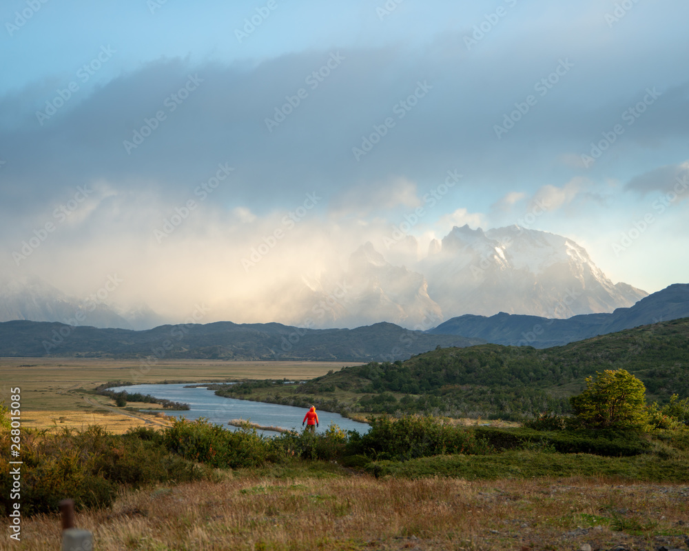 View of Mountains, grass meadow, and river during sunrise in Patagonia Chile, Torres del Paine  with lone figure in distance 