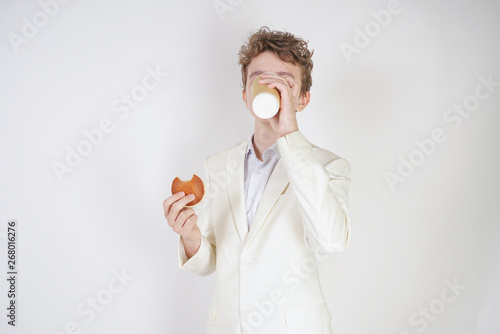 young student guy in a business suit stands with a Cup of coffee and cookies in his hands on a white background in the Studio