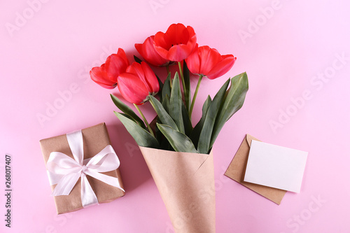 Fresh flower composition, bouquet of red color tulips, paper textured background with present. International Women's day, mother's day greeting concept. Copy space, close up, top view, flat lay.