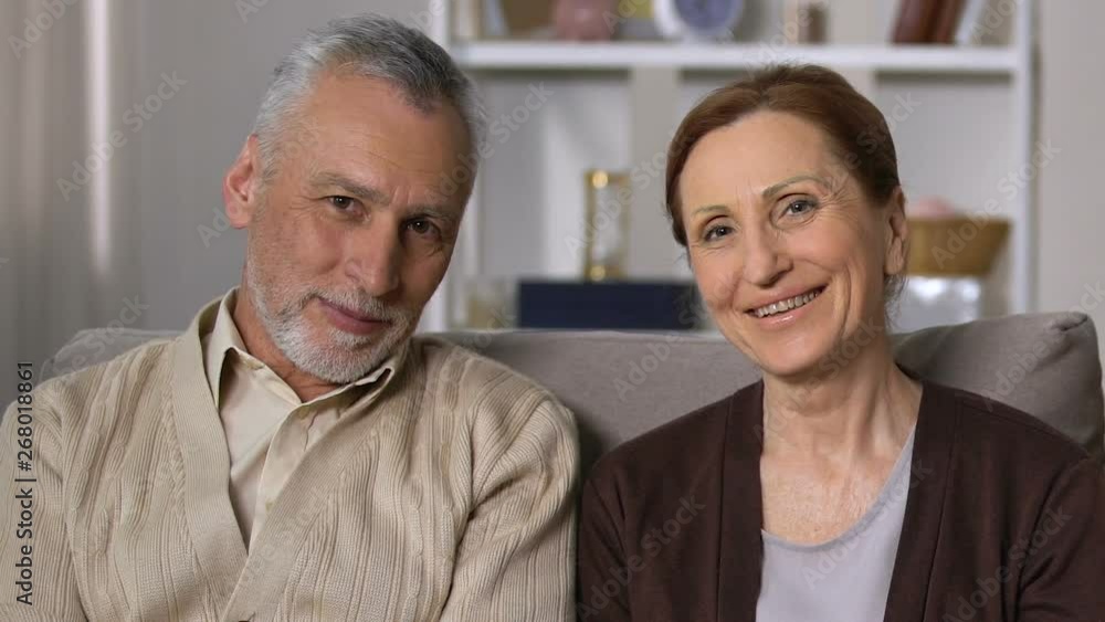 Happy retired couple looking camera sitting sofa, old age vitality, health Happy retired couple looking camera sitting sofa, old age vitality, health