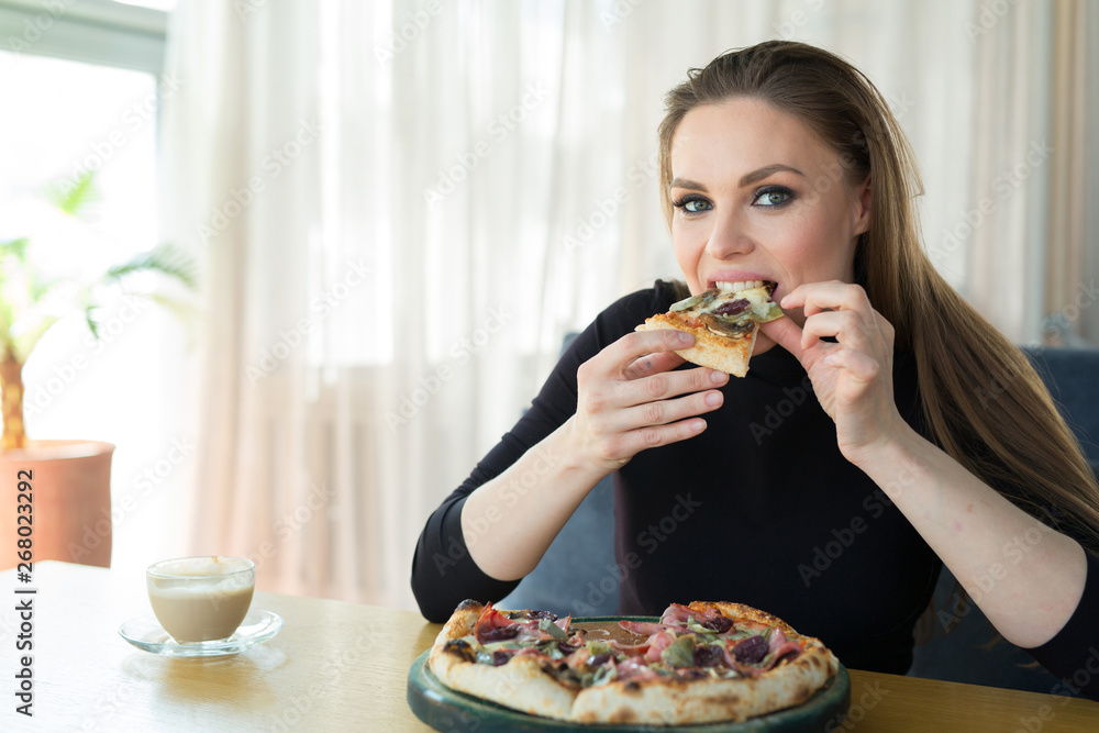 beautiful young woman at the table eats pizza in a restaurant beautiful young woman at the table eats pizza in a restaurant