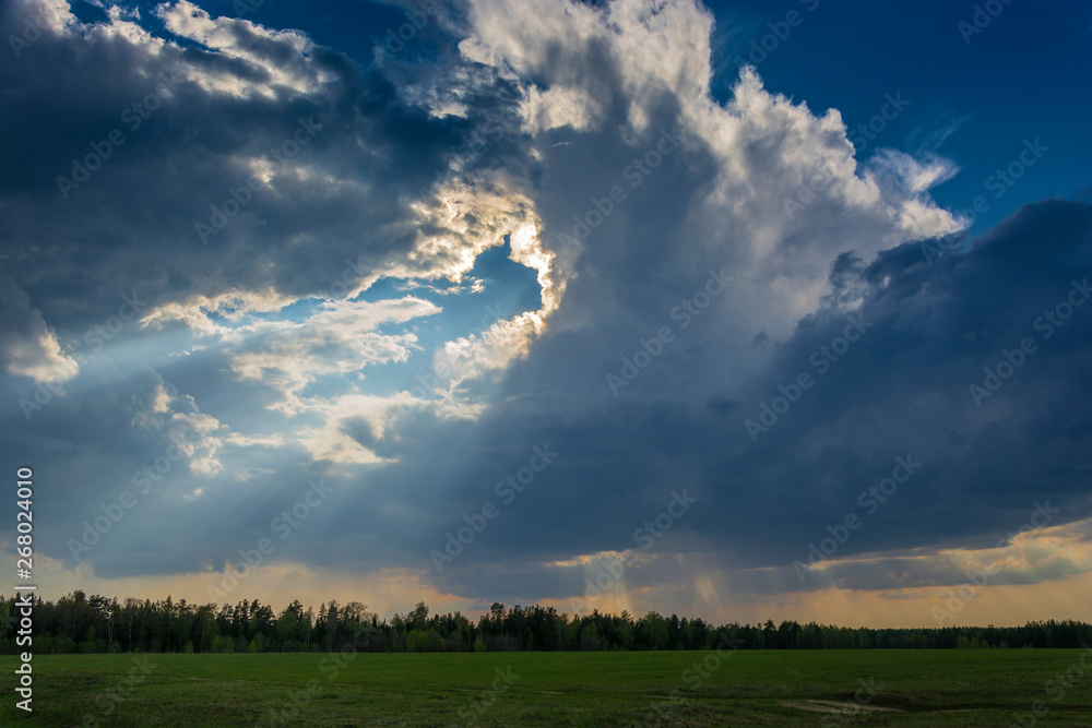 Beautiful landscape with a thundercloud and sunshine over a green field. Beautiful landscape with a thundercloud and sunshine over a green field.