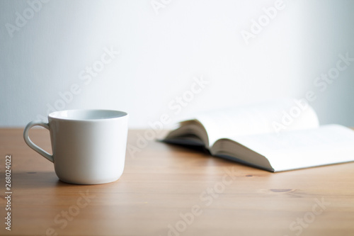 white coffee mug on wooden table and light background with book close up