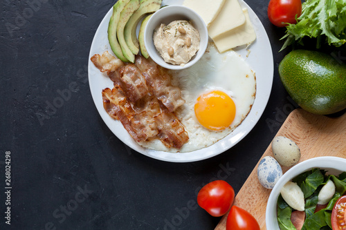 Keto breakfast with fried eggs, bacon, avocado, butter, hummus and vegetables. Healthy fats concept