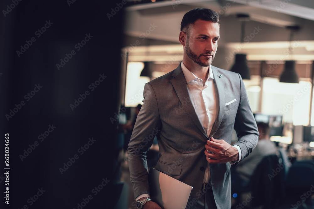 Attractive businessman standing in the office with his laptop