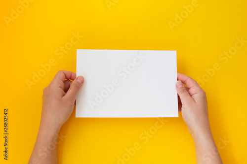 Hands holding blank white, empty paper isolated on yellow with copy space