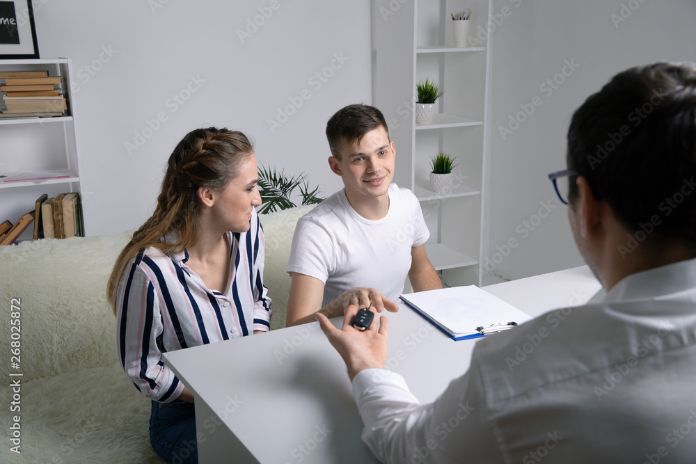 Obraz premium Beautiful happy couple bought a car in the dealership and receives the keys from the manager.