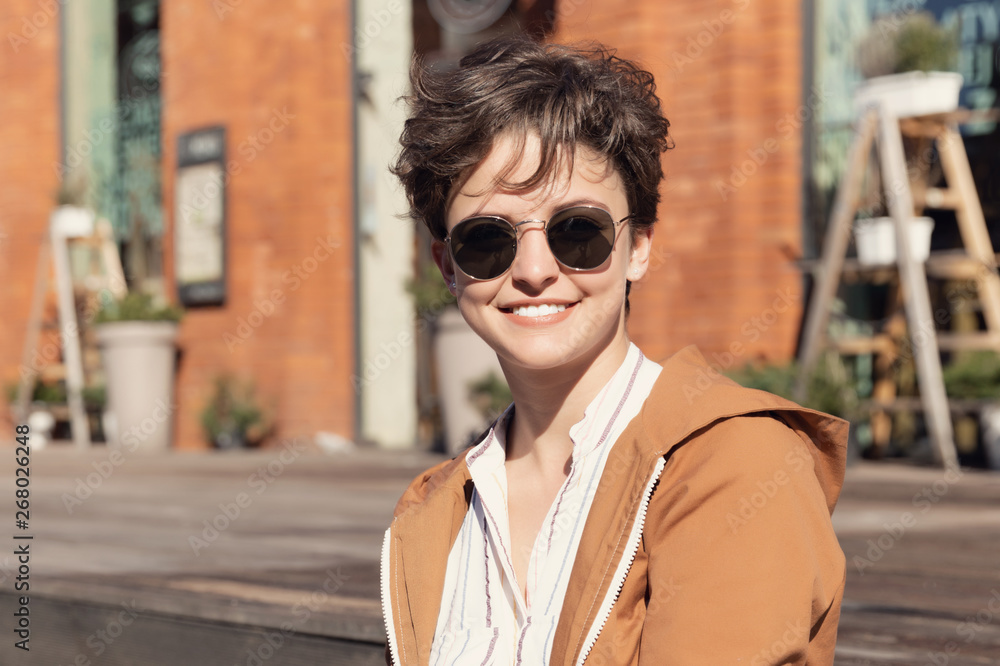 Young beautiful girl with a stylish haircut sitting on the street against a red brick wall. Young beautiful girl with a stylish haircut sitting on the street against a red brick wall.