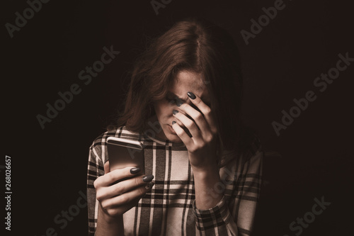 Fotografia Sad teen being victim of cyber bullying online sitting on a couch in the living