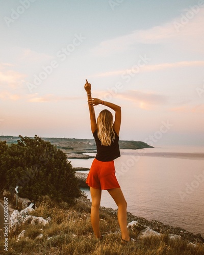 woman in black sleeveless top with red short shorts standing on hill near body of water