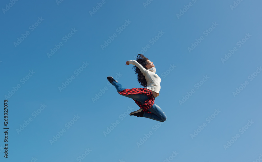 Modern young street dancer jumping high on a blue sky background. Woman flies up to the sun Modern young street dancer jumping high on a blue sky background. Woman flies up to the sun