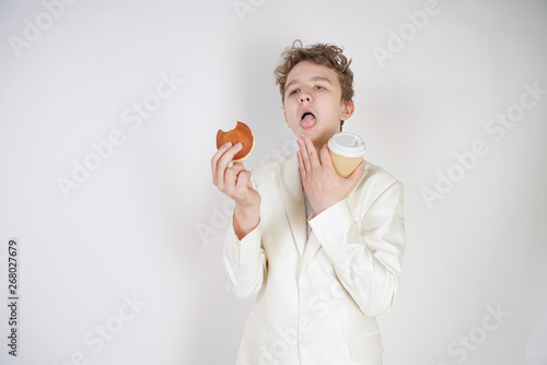 Young sad student guy in a business suit stands with a Cup of coffee and cookies in his hands on a white background in the Studio