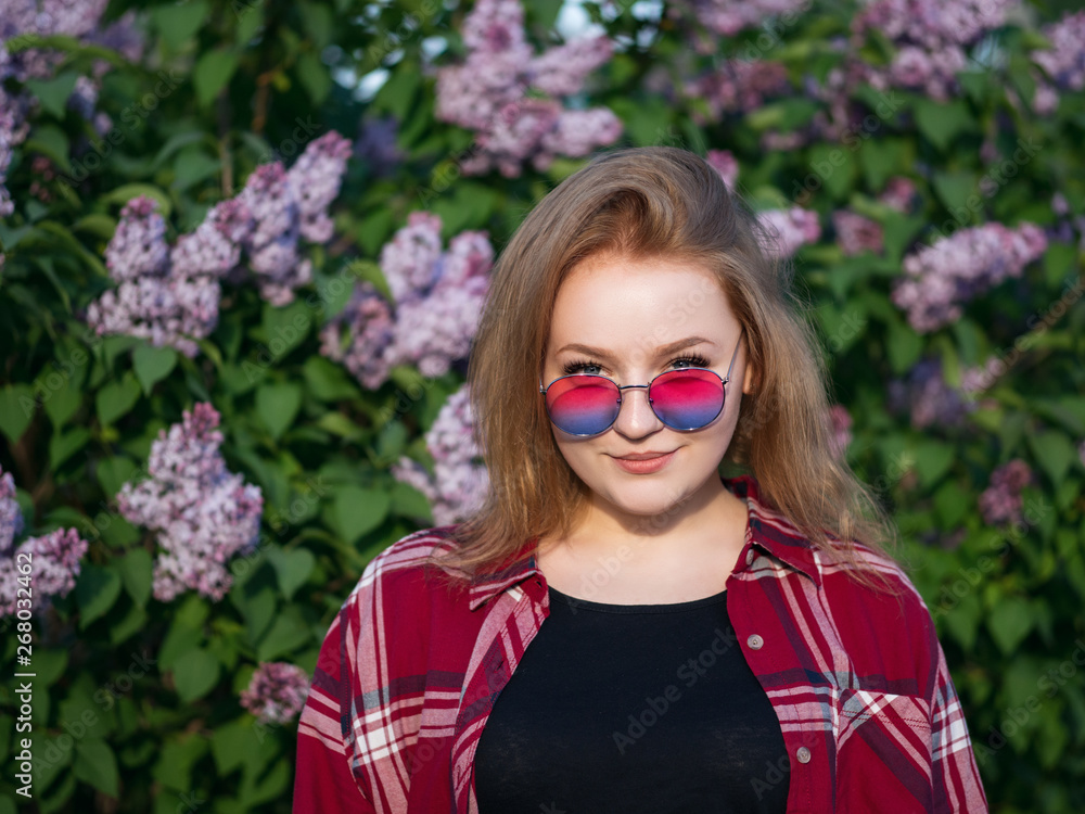 Close-up portrait of an attractive girl in colorful sunglasses on a background of blooming lilac Close-up portrait of an attractive girl in colorful sunglasses on a background of blooming lilac