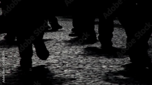 People walking on the city street sidewalk in black and white. Silhouettes of walking multiple people legs on cobblestone ground. A urban landscape concept.