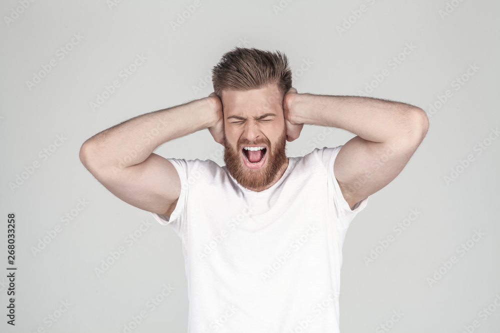 Portrait of beautiful sexy bearded man. holds his arms behind his head and shouts. he has a headache, he stands in front of the white background Portrait of beautiful sexy bearded man. holds his arms behind his head and shouts. he has a headache, he stands in front of the white background