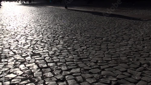People walking on the city street sidewalk in black and white. Silhouettes of walking multiple people legs on cobblestone ground. A urban landscape concept.
