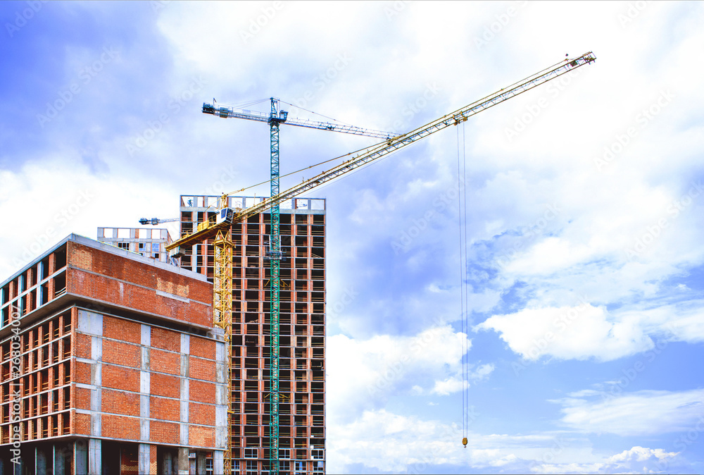 Construction site of residential buildings with unfinished facade anf huge cranes against the sky with copy space for text.