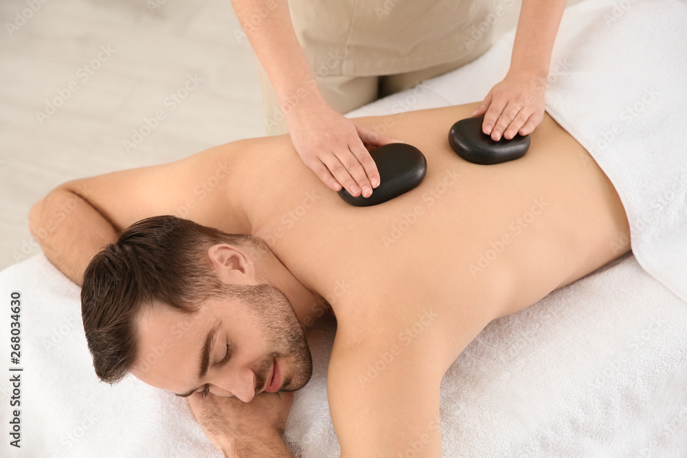 Handsome man receiving hot stone massage in spa salon, above view Handsome man receiving hot stone massage in spa salon, above view