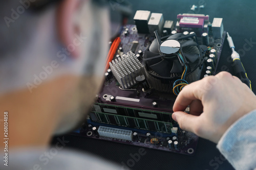 Male technician repairing motherboard at table, closeup
