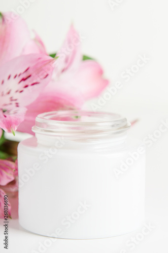 Face cream in white jar on a white background with pink flowers. Concept natural cosmetics  organic beauty  flower arrangement. Copy space.