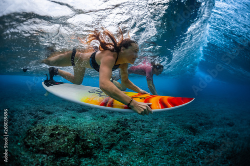 Two young surfers man and woman dive with their surfboards under the breaking ocean wave