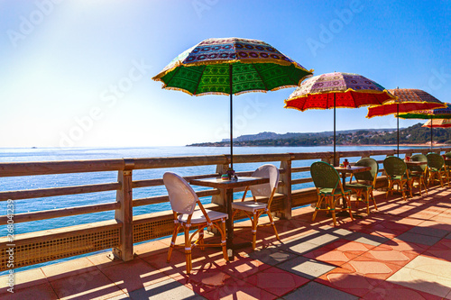 Multi-colored umbrellas against the background of the sea in coastal cafe limited by a wooden handrail.