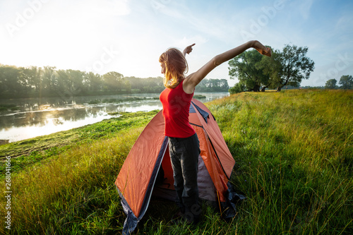 Young woman hiker stretches near the tent and greets the sun photo