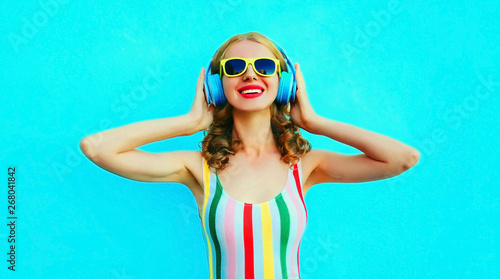 Portrait happy smiling woman listening to music in wireless headphones on colorful blue background