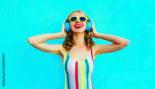 Portrait happy smiling woman listening to music in wireless headphones on colorful blue background