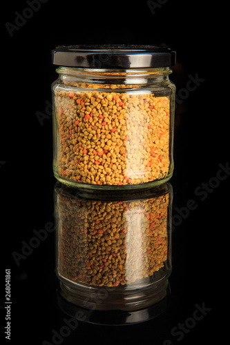 small glass jar with bee pollen on black background