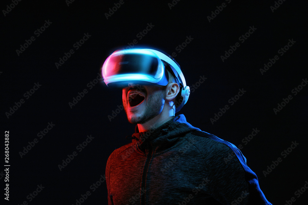 Model young man with beard in glasses of virtual reality on dark background.. Augmented reality, science, future technology concept. VR. Futuristic 3d glasses with virtual projection. Neon light. Model young man with beard in glasses of virtual reality on dark background.. Augmented reality, science, future technology concept. VR. Futuristic 3d glasses with virtual projection. Neon light.